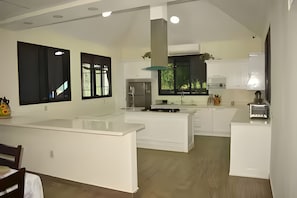 Une cuisine moderne avec des meubles blancs, un îlot central et une grande fenêtre qui laisse entrer la lumière naturelle.