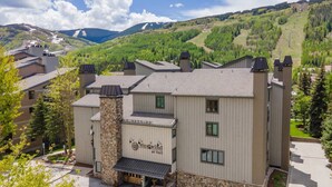 A multi-story building with a stone chimney, a sign reading "WestWind at Vail," and a view of a mountainous landscape in the background. - Free Parking, Pool, Hot Tub, near Gondola | W301 (Vail)