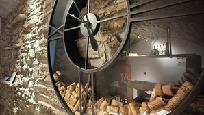 Eine runde Wanduhr mit römischen Ziffern vor einer rauen Steinwand.
