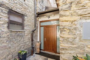 A stone building with a wooden door, a metal mesh window, and a potted plant.