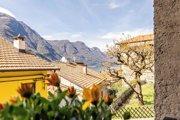 A yellow building with a tiled roof, a tree with yellow flowers, and mountains in the background.