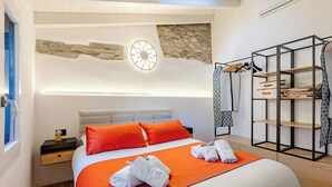 Ein modernes Hotelzimmer mit Bett, orangefarbener Bettwäsche, einer Wand mit Steinakzenten, einer Wanduhr und einem eingebauten Kleiderschrank.