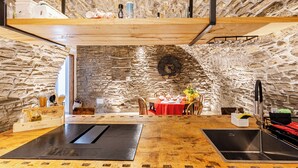 Ein rustikales Steinambiente mit Essbereich, Holztischen und einer Küche mit Spüle und Wasserhahn.