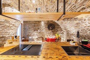 A rustic stone interior with a dining area, wooden tables, and a kitchen with a sink and faucet.