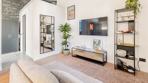 Ein modernes Wohnzimmer mit Steinwand, großem Fernseher, einer Couch, einem Konsolentisch und einer Pflanze.