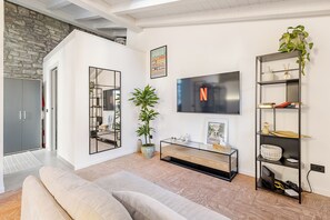A modern living room with a stone wall, a large TV, a sofa, a console table, and a plant.