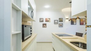 A compact kitchen with white cabinets, a microwave, a sink, and a countertop with a tablet. - Complete Apartments in Asa Norte - BSB BVT (Brasília)