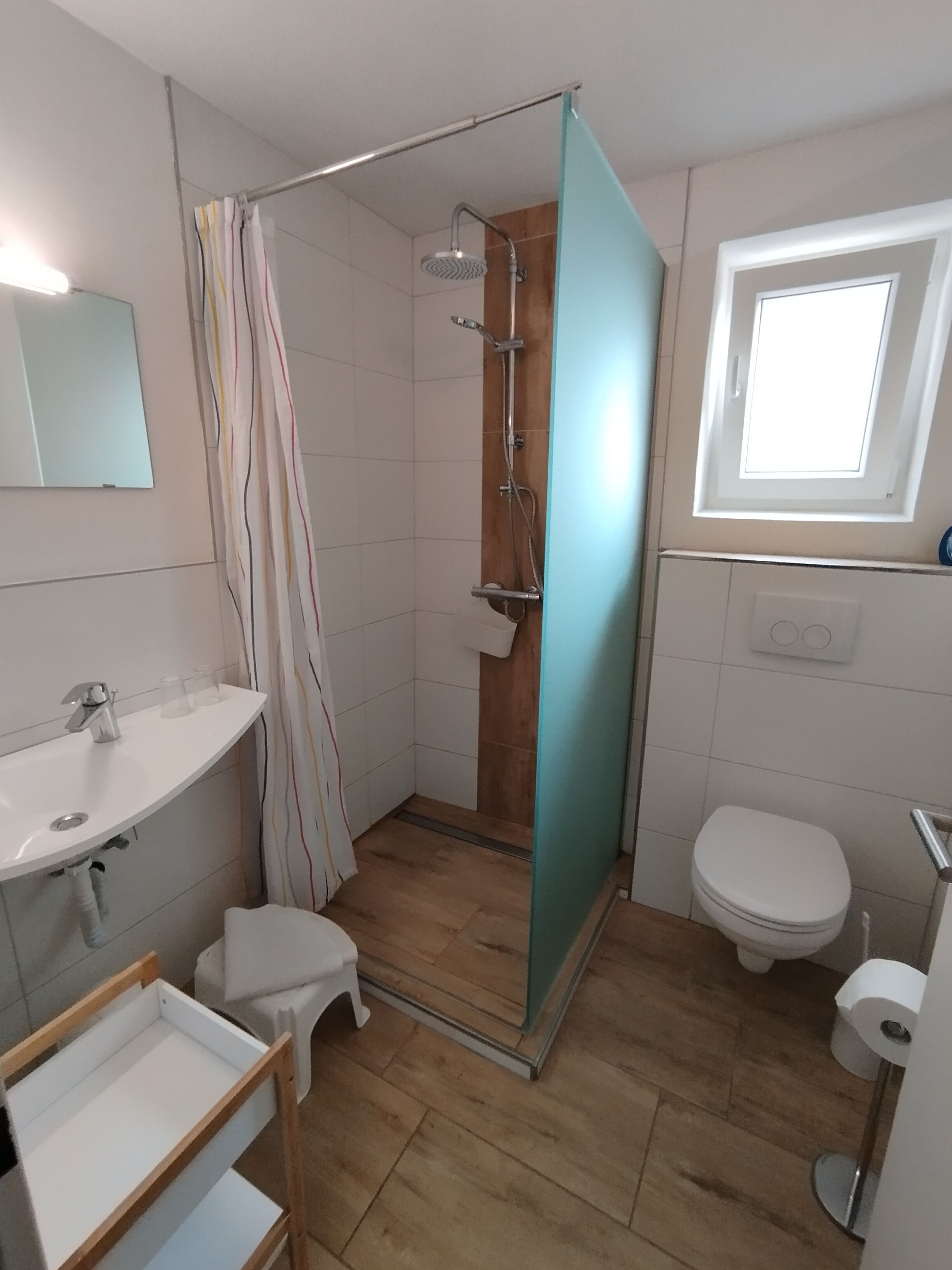 Ein Badezimmer mit Dusche, Toilette, Waschbecken und einem Fenster.