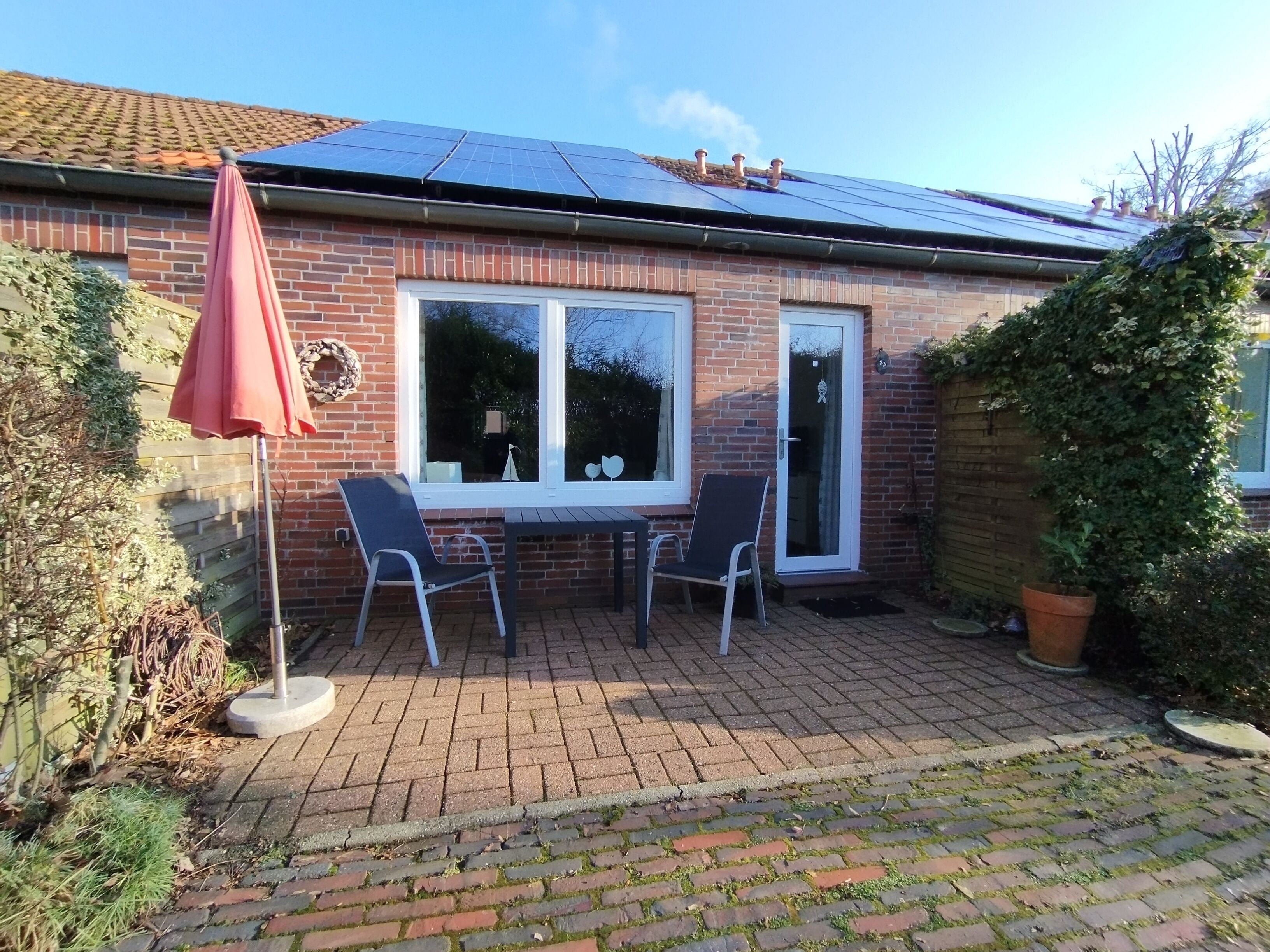 A brick house with a tiled roof, two windows, a door, and a patio area with two chairs and a table.
