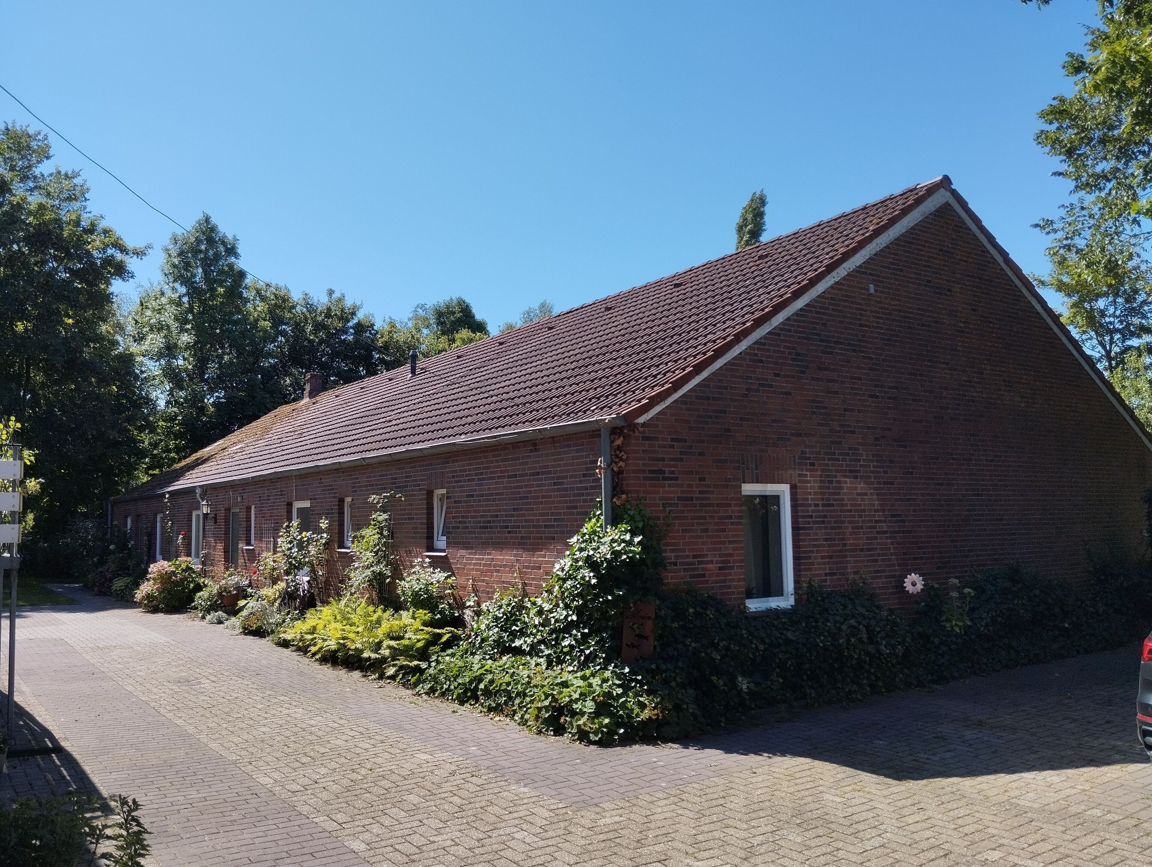 Een bakstenen gebouw met een schuin dak, een verharde oprit en omliggend groen.
