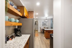 Une cuisine moderne avec des étagères en bois, un réfrigérateur, une machine à café et un coin repas comprenant une table et des chaises.