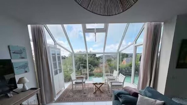 Ein modernes Wohnzimmer mit einer Couch, einem Couchtisch und einem Fernseher. Eine Glastür führt zu einer Terrasse mit Pool und Stühlen.