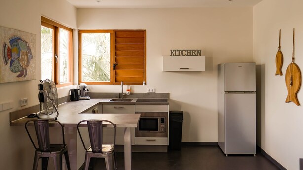 Une cuisine compacte équipée d’un four encastré, d’un four à micro-ondes et d’un réfrigérateur. Elle comprend également un coin repas avec deux chaises et une table.