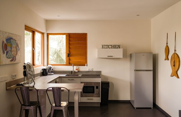 Uma cozinha compacta com forno embutido, micro-ondas e frigorífico. Possui uma área de jantar com duas cadeiras e uma mesa.