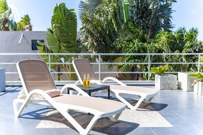 Eine Dachterrasse mit zwei Liegestühlen, einem kleinen Tisch und zwei Bierflaschen.