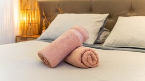 Un lit bien fait, avec deux serviettes enroulées et une lampe sur une table de chevet.