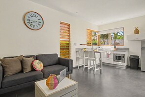 A modern living room with a grey sofa, a colorful woven basket, and a wall clock. - Villa Sol Paraiso Deluxe (Jan Thiel)
