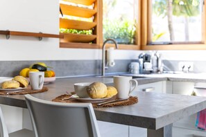 Eine moderne Küche mit Essbereich, ausgestattet mit einer Kücheninsel, einer weißen Tasse, einem Teller mit Keksen und einer Schüssel mit Obst.