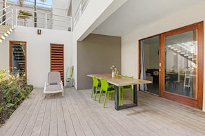 Eine moderne Terrassengrundstueck mit einem Holztisch und -stuehlen, einer Schiebetuer und einem Balkon mit Geländer.