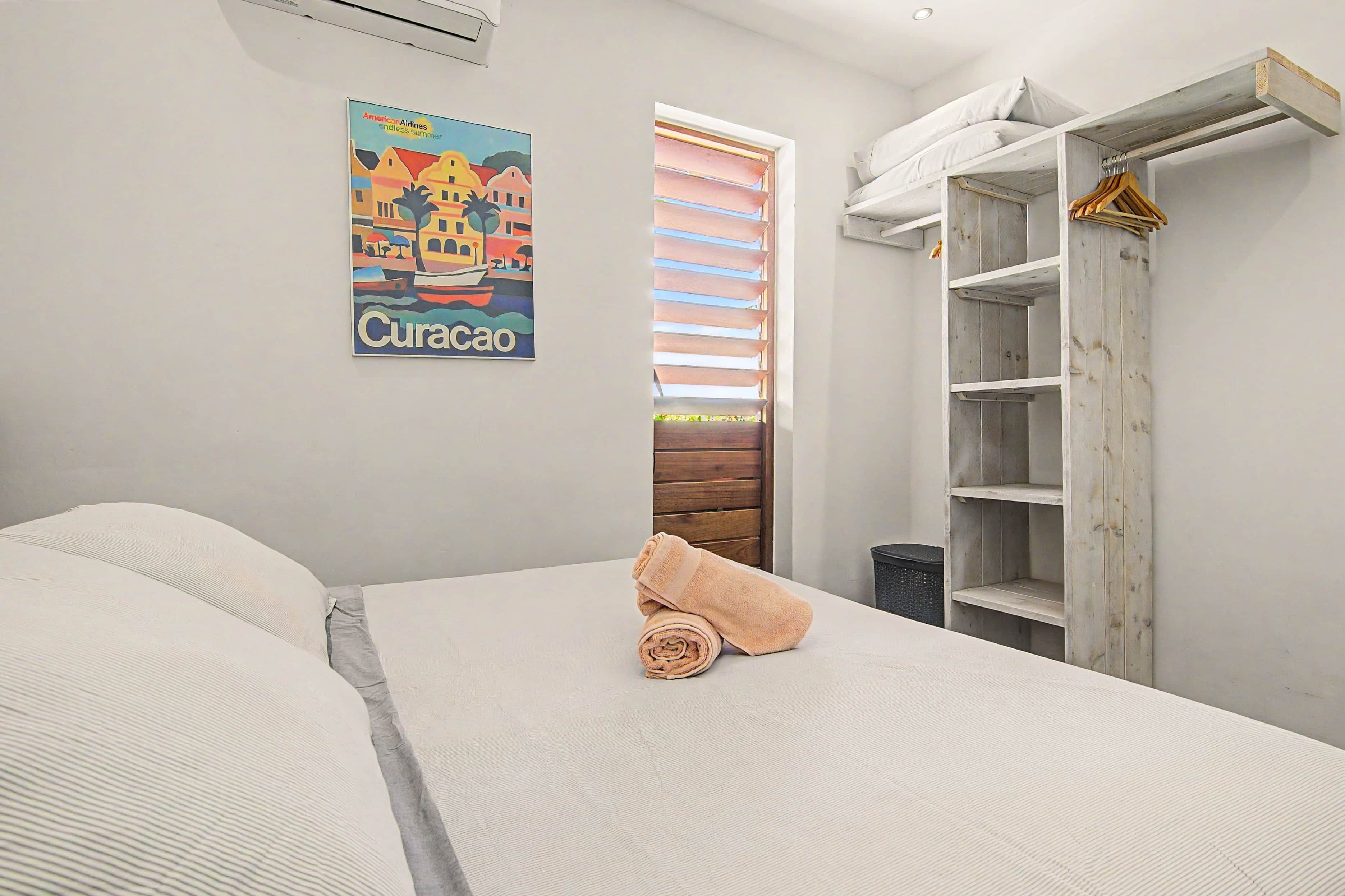 A bedroom with a bed, a rolled towel, a wardrobe, and a window with blinds.