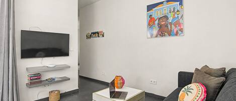 A modern living room with a flat-screen TV, a sofa, a coffee table with a laptop, and a wall with a colorful poster.