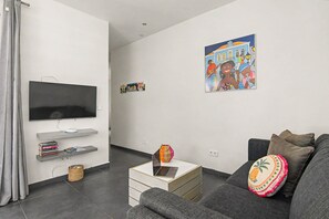 En moderne stue med et fladskærms-tv, en sofa, et sofabord med en bærbar computer og en væg med et farverigt plakat.