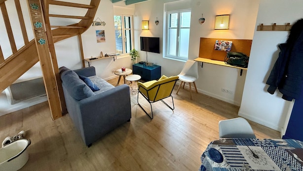 A cozy living room with a wooden spiral staircase, a sofa, a small table, and a TV. - House just a stone's throw from the sea (Saint-Gilles-Croix-de-Vie)