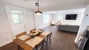 A modern kitchen with a dining area, wooden flooring, and a TV mounted on the wall. - The Downtown Cedar (Ocean Springs)