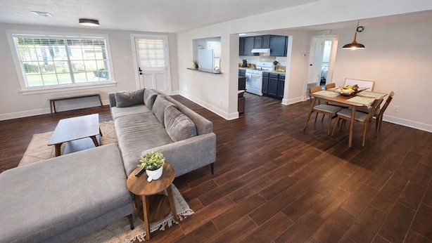 A spacious living area with a grey sofa, a round wooden coffee table, and a dining table with chairs. - The Downtown Cedar (Ocean Springs)