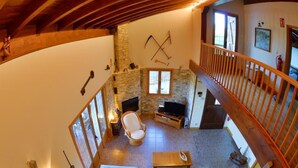 Ein gemütliches Wohnzimmer mit Kamin aus Stein, einer Couch, einem Fernseher und einer Holztreppe.