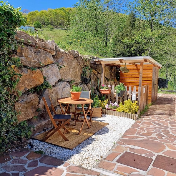 A rustic wooden cabin with a stone pathway leading to a wooden deck with a table and chairs.