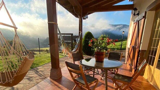 Eine überdachte Terrasse mit Tisch und Stühlen, einem Hängesessel und Blick auf die Berge.