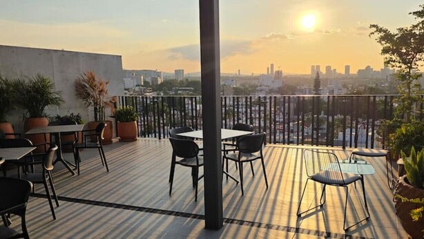 En tagterrasse med borde, stole, plantekasser og udsigt over bybilledet i solnedgang.