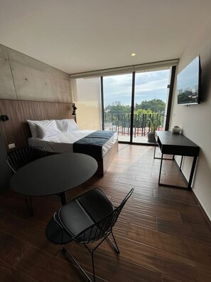 Ein modernes Hotelzimmer mit Bett, kleinem Tisch, zwei Stühlen, einem Balkon mit Blick und einem Wand-Fernseher.