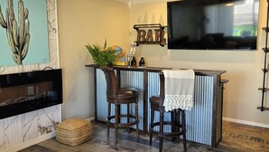 Ein Wohnzimmer mit Deckenventilator, Fernseher, Barbereich und einem großen Kaktusgemälde.