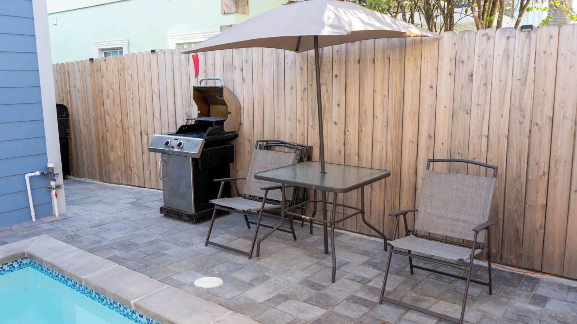 Une terrasse extérieure équipée d’un barbecue, d’une table et de chaises, située à côté d’une piscine.