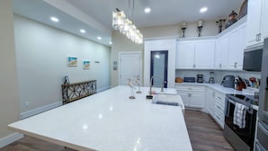 A modern kitchen with white cabinetry, a central island, and a hanging light fixture. - Steps to Beach Private Pool 2 Big Levels (South Padre Island)
