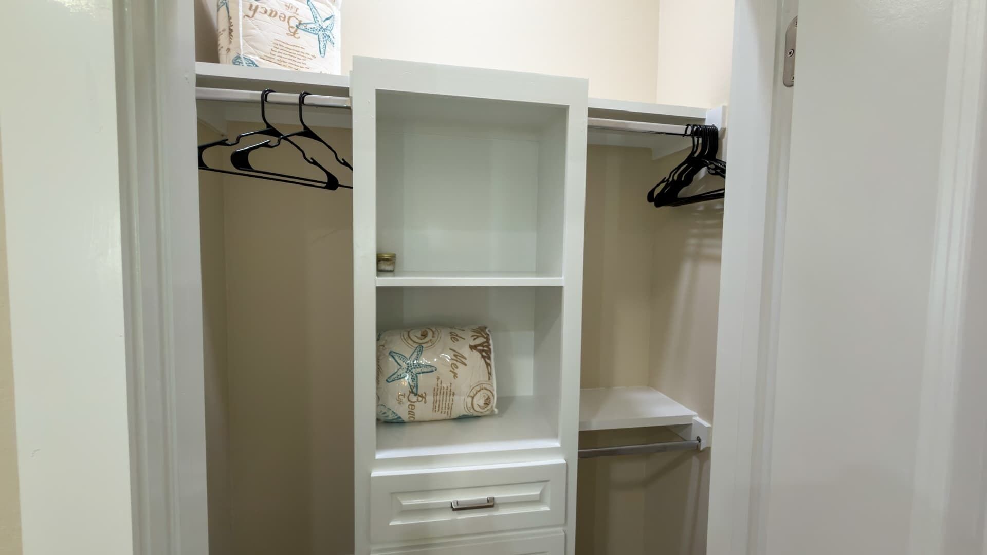 Un armario blanco con puertas abiertas, que incluye estantes, una barra para colgar ropa y un cajón.