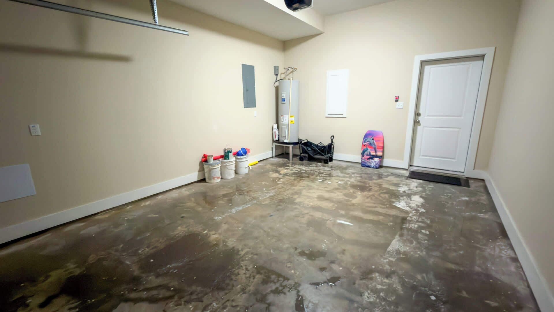 Ein Zimmer mit nassen Böden, was auf kürzlich durchgeführte Arbeiten oder Reinigung hindeutet. Eimer und eine Leiter lehnen an der Wand, was laufende Instandhaltungs- oder Renovierungsarbeiten andeuten.
