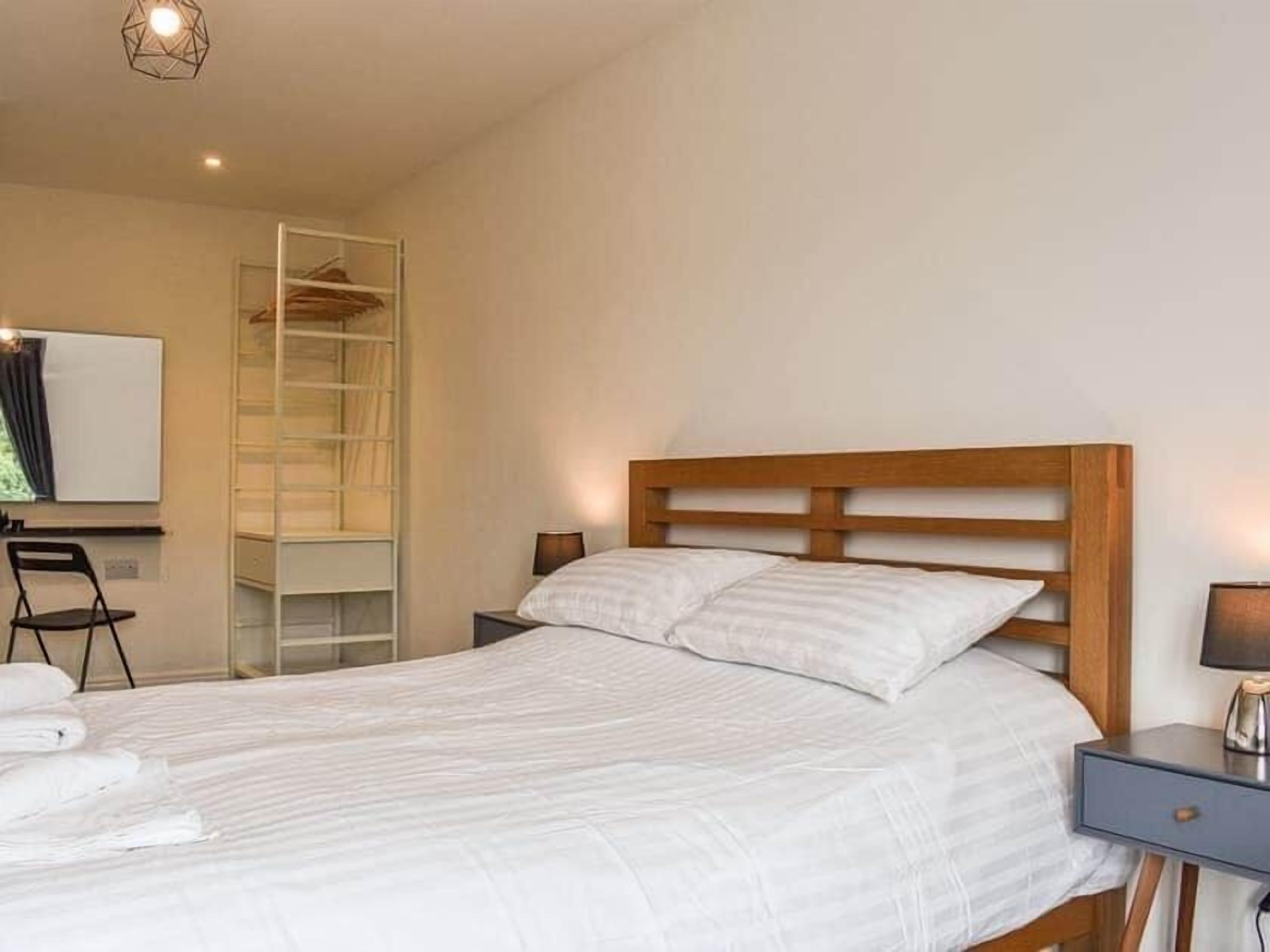 Una cama bien hecha con cabecera de madera, una mesita de noche con lámpara y un armario empotrado.