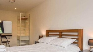 Uma cama bem arrumada com cabeceira de madeira, uma mesa de cabeceira com abajur e um guarda-roupa embutido.