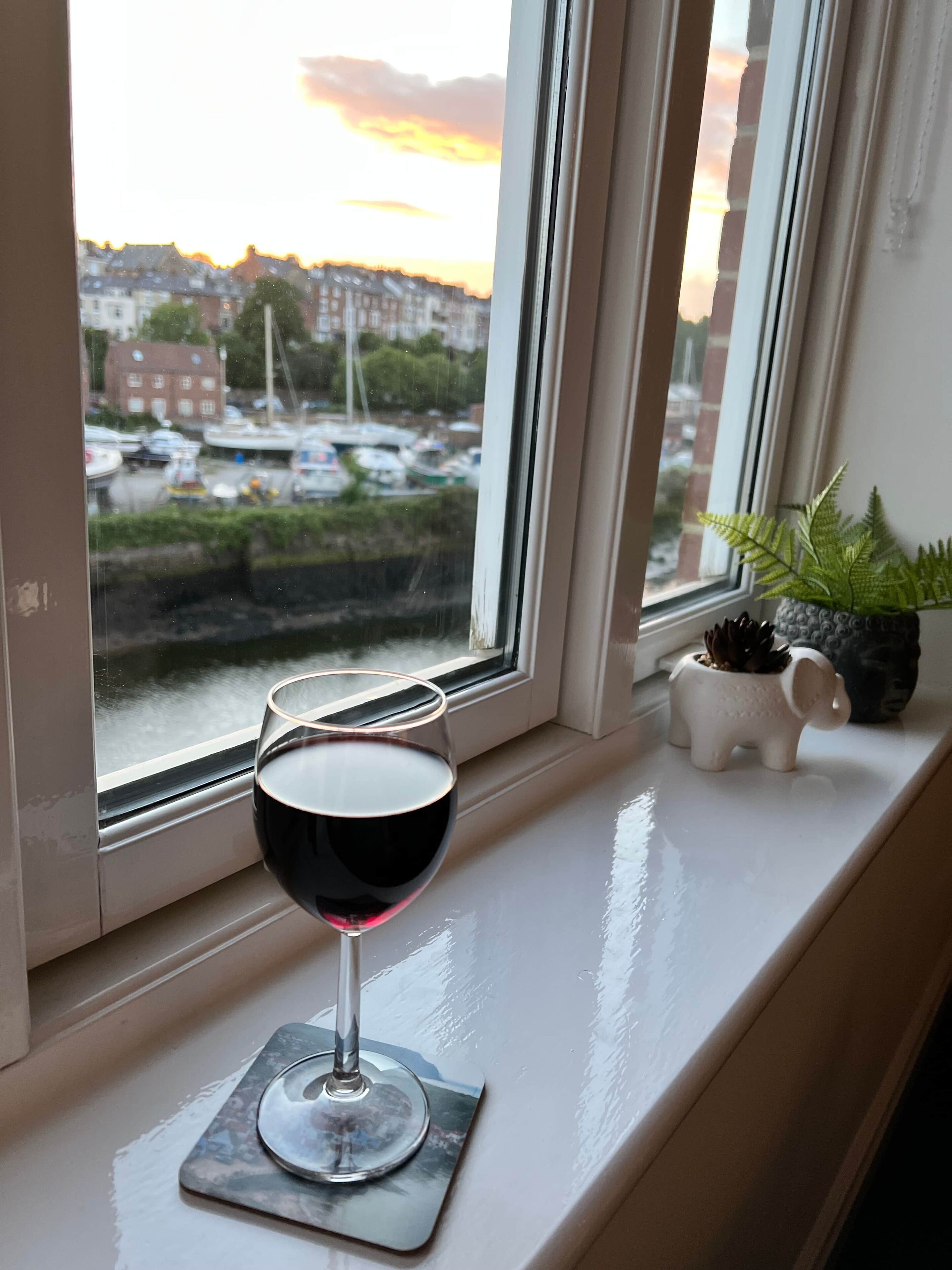 Un bicchiere di vino rosso su un davanzale con vista su un porto turistico e edifici.