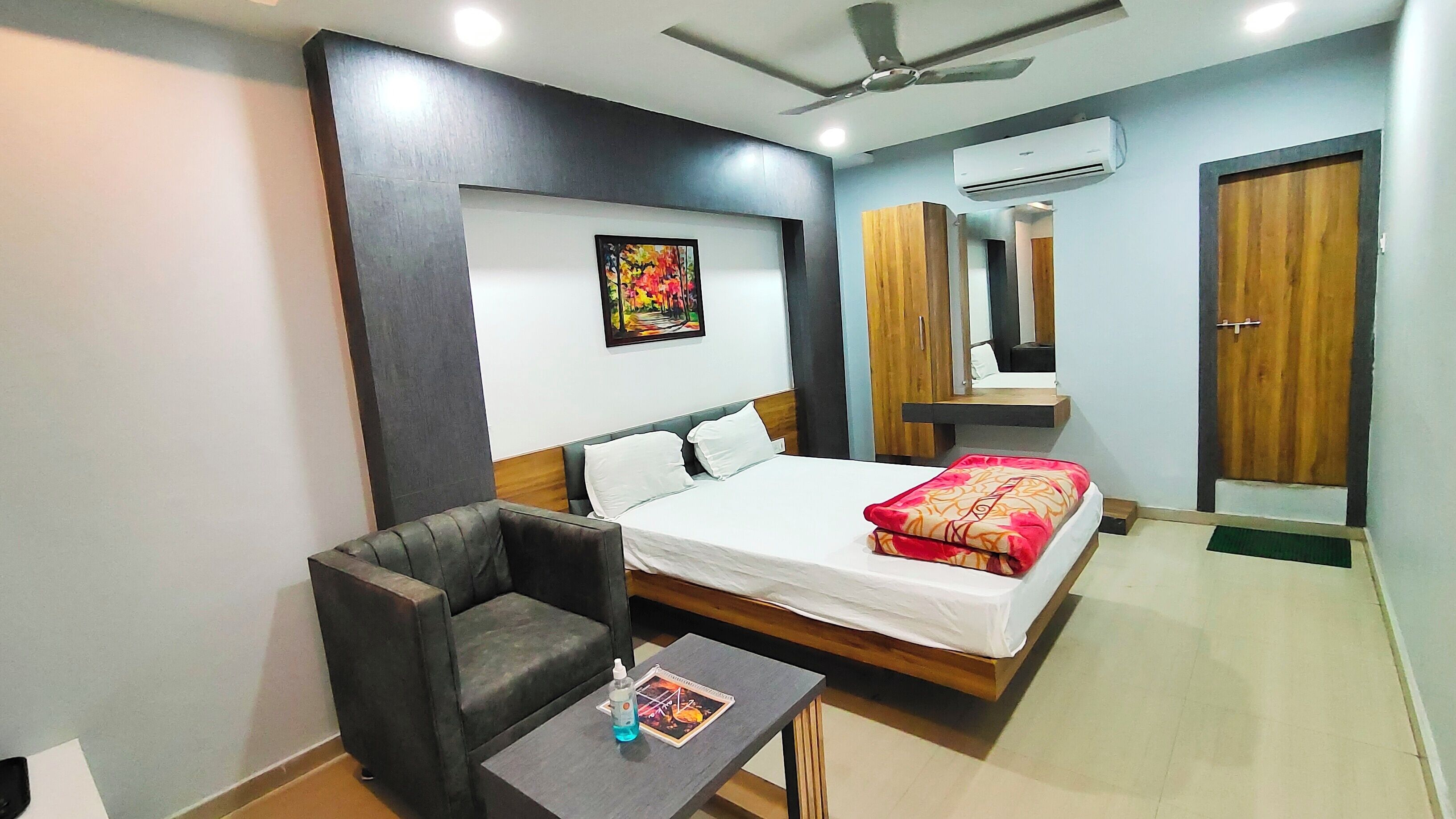 A hotel room with a bed, a chair, a small table, a wall-mounted air conditioner, and a door.