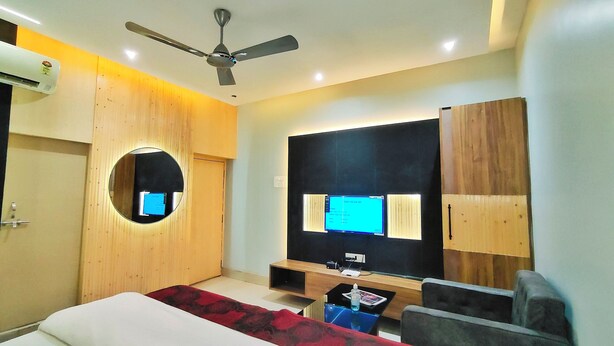 A modern hotel room with a bed, a round mirror, a ceiling fan, a flat-screen TV, and a wooden wardrobe. - Hotel Jay Deluxe (Sasaram)
