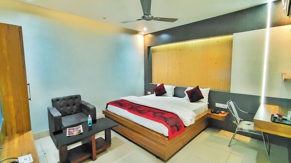 A modern hotel room with a large bed, a desk, a chair, and a ceiling fan. - Hotel Jay Deluxe (Sasaram)