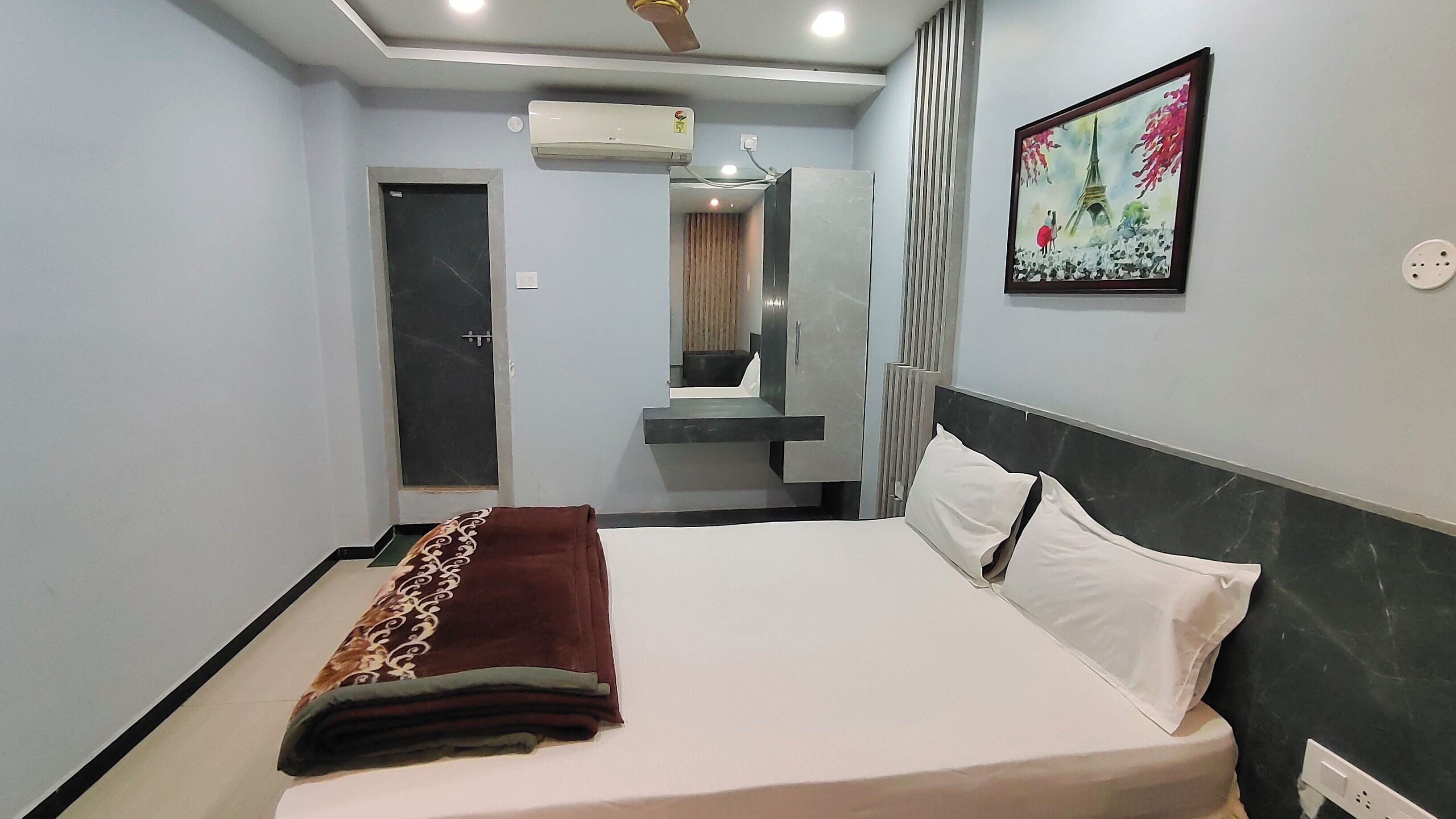 A modern hotel room with a bed, a mirror, a painting, and a ceiling fan.