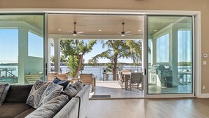 Un salón moderno con un amplio ventanal corredero que da a un patio exterior con vistas al agua y árboles.