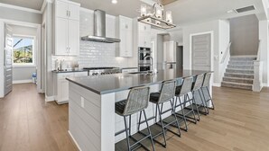 Una cocina moderna con armarios blancos, una isla grande con taburetes de bar, electrodomésticos de acero inoxidable y una lámpara colgante.