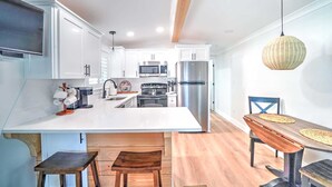 Una cocina moderna con armarios blancos, electrodomésticos de acero inoxidable, una isla de madera y un comedor con mesa y sillas de madera.
