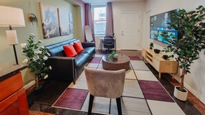 A modern living room with a sofa, coffee table, TV, and decorative plants. - Vale / King Bed / Elevator / Balcony / Ensuite (Philadelphia)